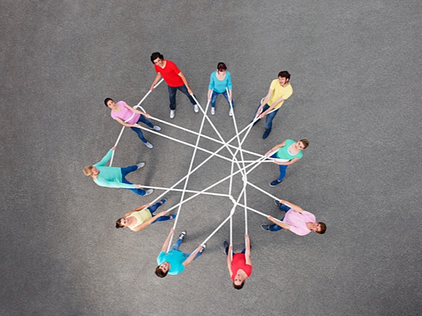 Group of people stand in a circle connected by a long tangled piece of string